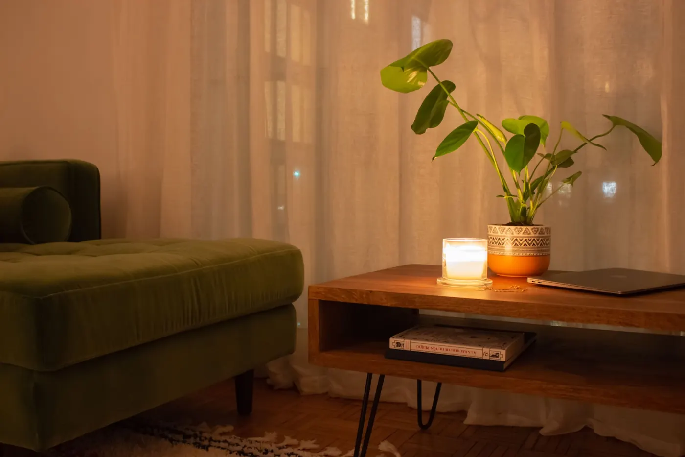 Rincón de salón con sofá verde, mesa baja de madera, vela y planta