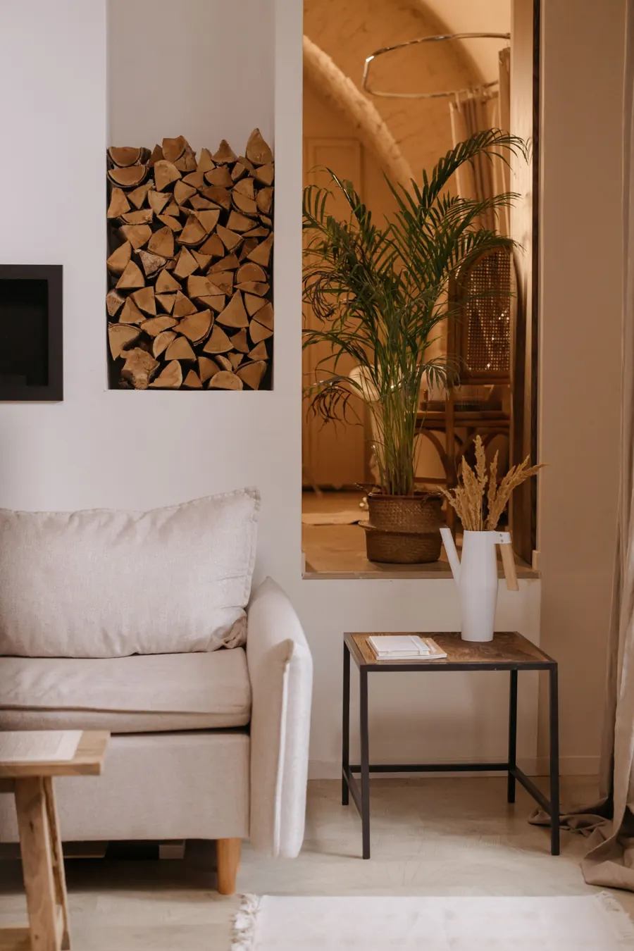 Salón pequeño con sofá beige y una mesa auxiliar de metal junto a la pared